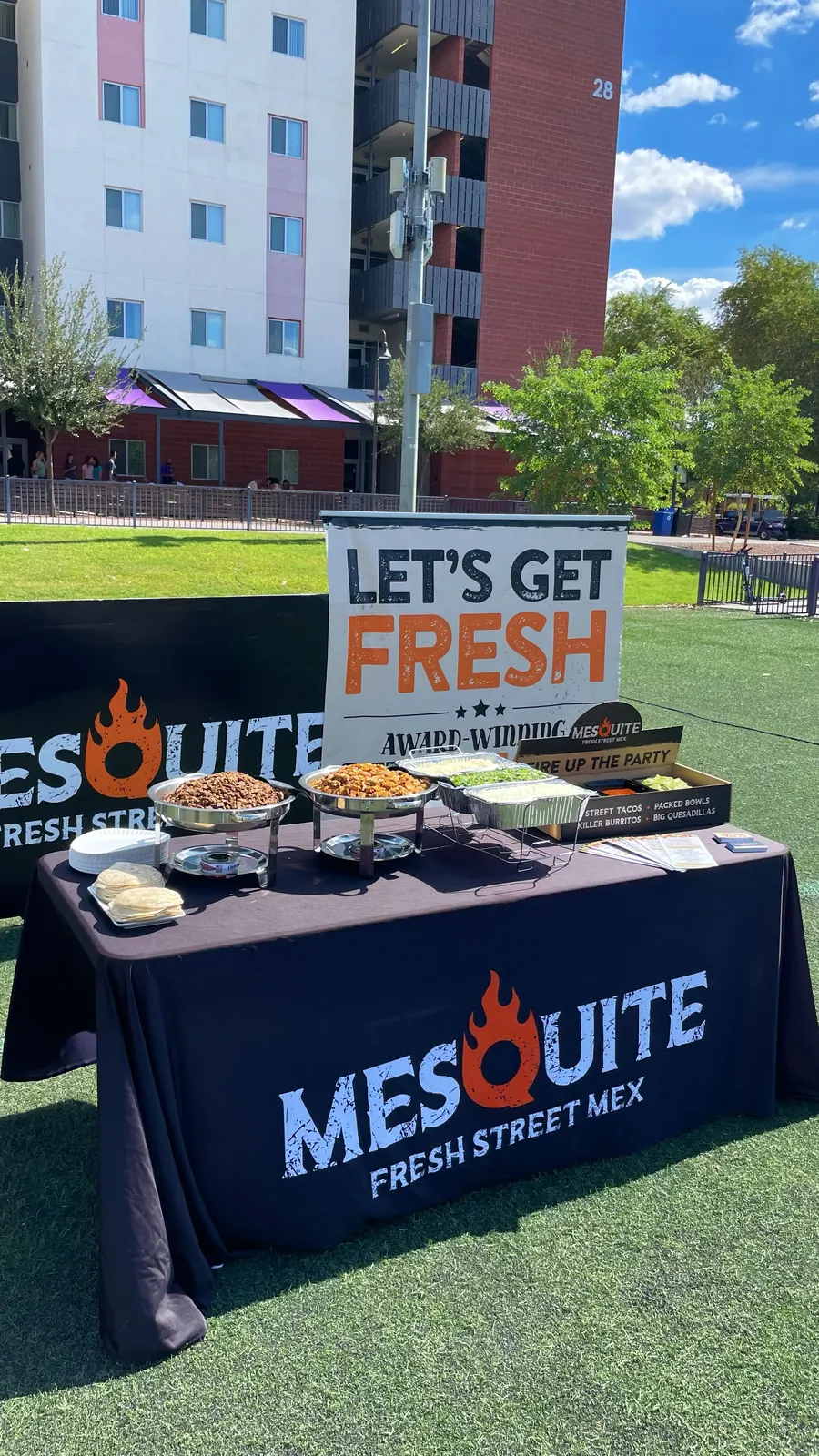 Mesquite Fresh Street Mex catering table set up outdoors at a campus event with chafing trays, tortillas, and a Let’s Get Fresh banner