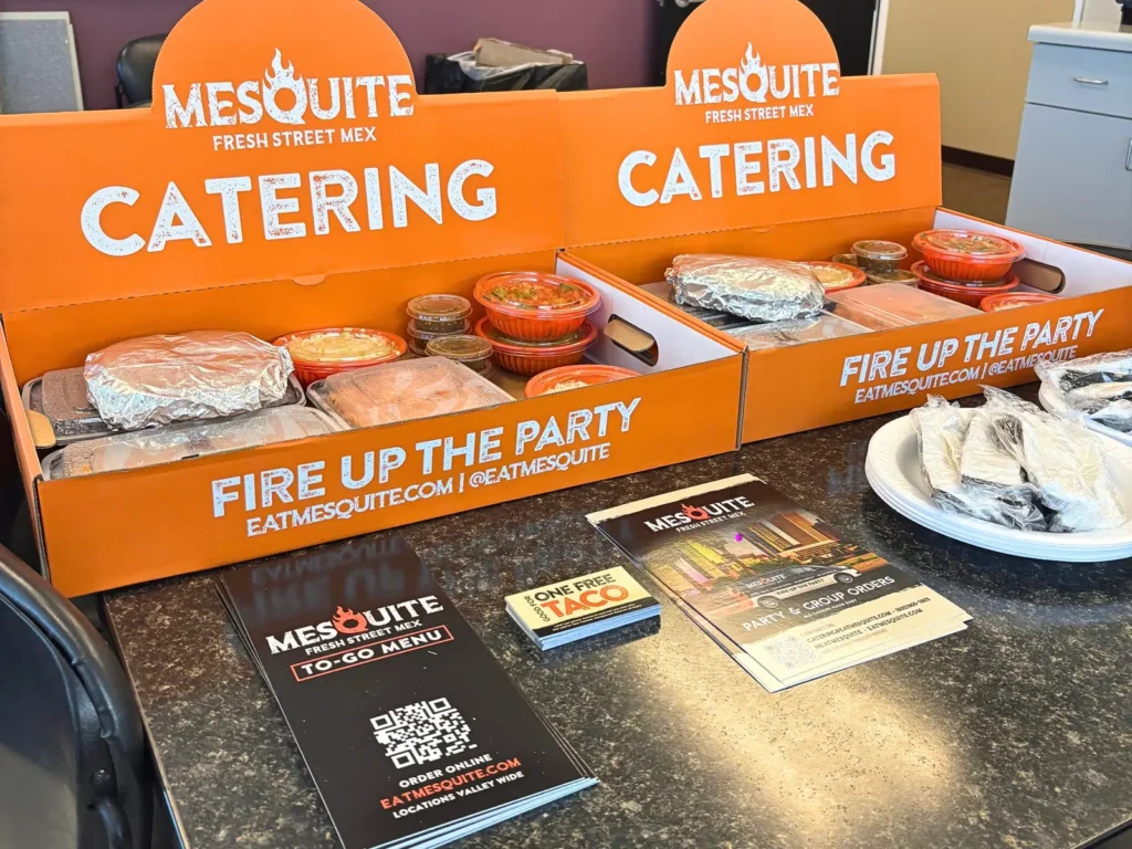 Two Mesquite catering boxes with to-go menus and free taco cards on a conference room table