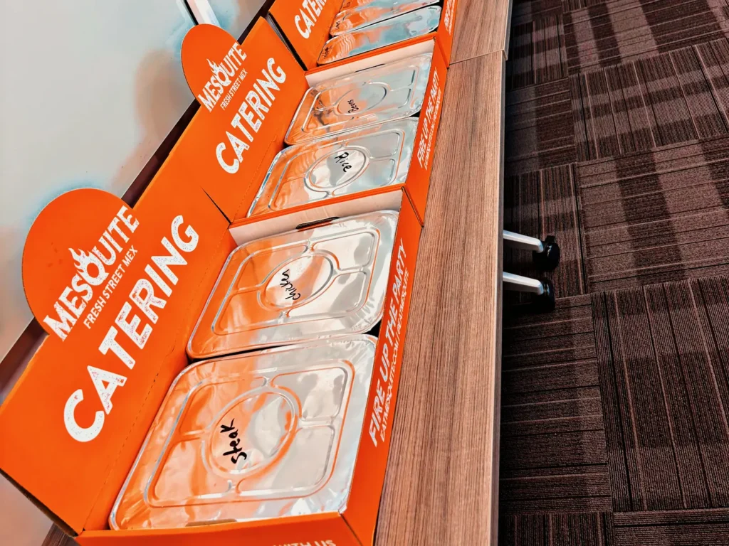 Row of Mesquite catering boxes with labeled steak, chicken, rice and bean trays